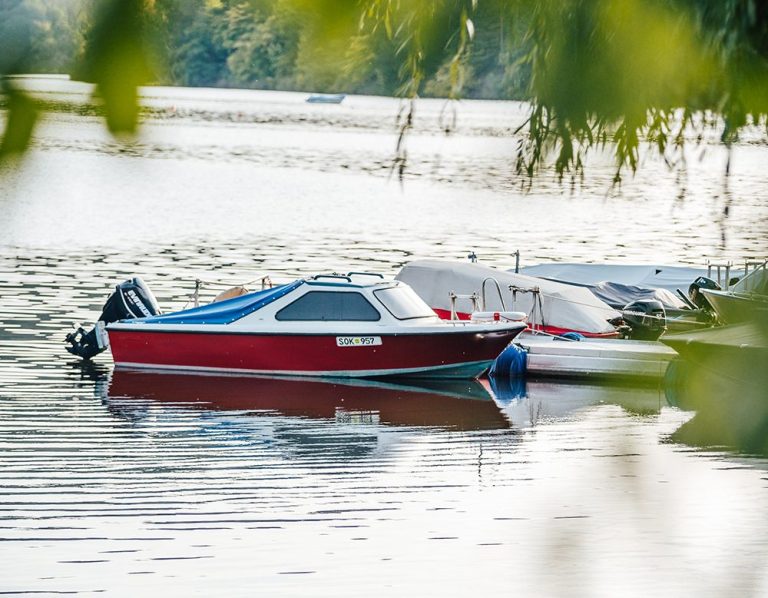 Boot Ein rotes Boot liegt ruhig am Ufer eines glitzernden Gewässer.